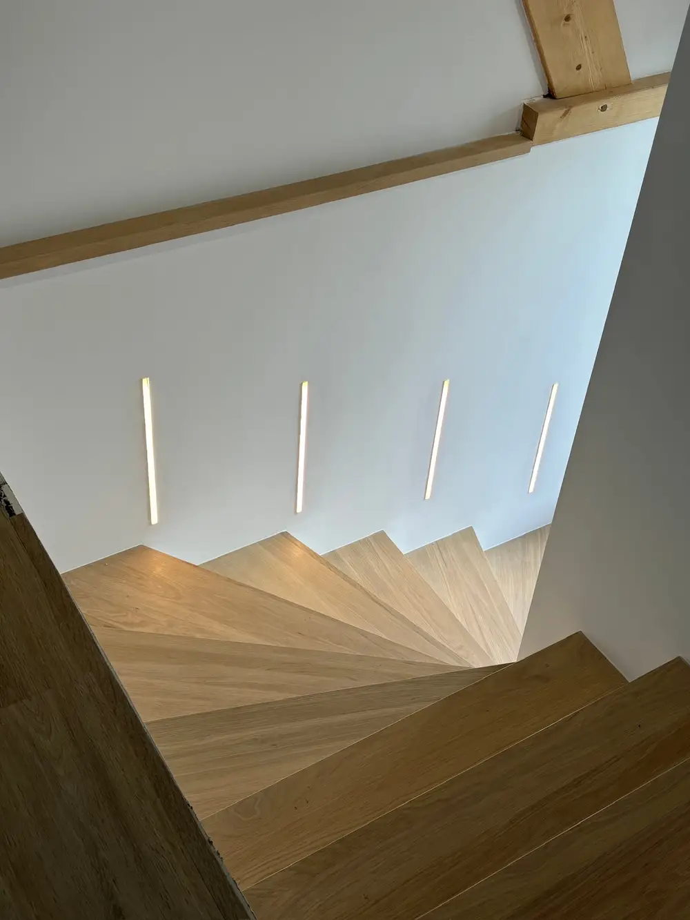 Réglettes LED encastrées dans le mur pour éclairer un escalier en bois